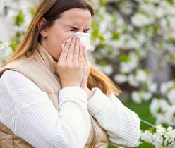 Woman with seasonal allergies sneezing outdoors in spring, highlighting common allergy symptoms and the need for effective management strategies.