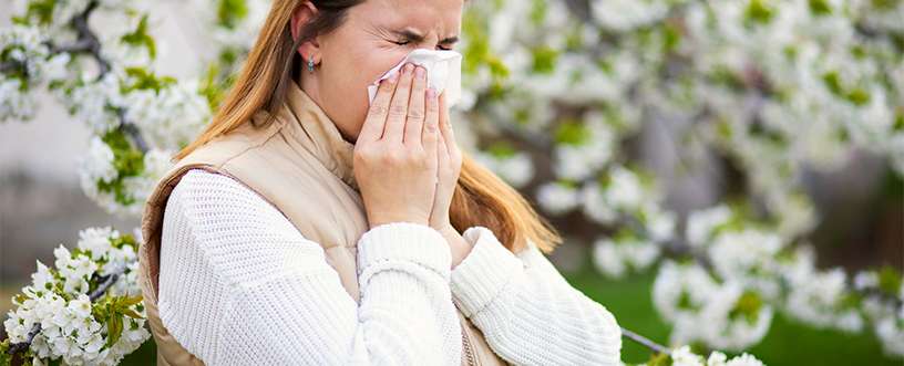 Woman with seasonal allergies sneezing outdoors in spring, highlighting common allergy symptoms and the need for effective management strategies.