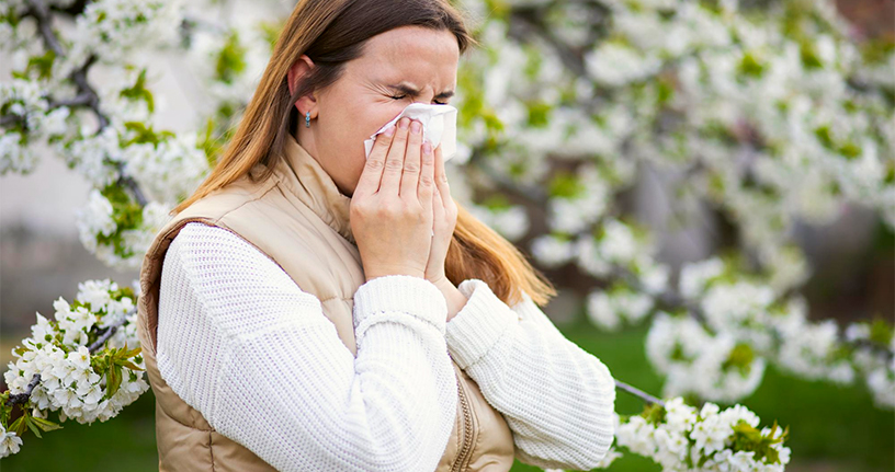 Woman with seasonal allergies sneezing outdoors in spring, highlighting common allergy symptoms and the need for effective management strategies.