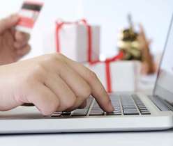 Close-up of a person entering a Reliable Rx Pharmacy coupon code on a laptop while holding a credit card, with gift boxes in the background