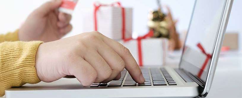 Close-up of a person entering a Reliable Rx Pharmacy coupon code on a laptop while holding a credit card, with gift boxes in the background