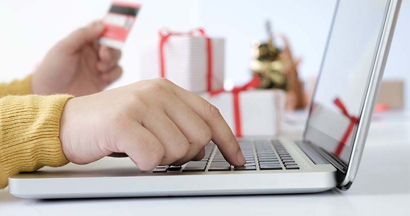 Close-up of a person entering a Reliable Rx Pharmacy coupon code on a laptop while holding a credit card, with gift boxes in the background